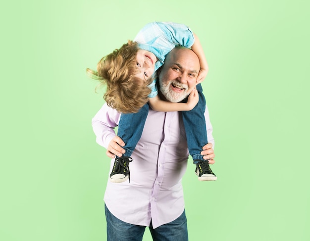 Old grandfather and young child grandson piggyback ride with\
funny face isolated elderly old relativ