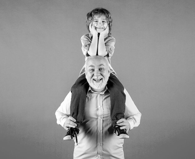 Old grandfather and young child grandson piggyback ride with funny face isolated on yellow Elderly old relative with child