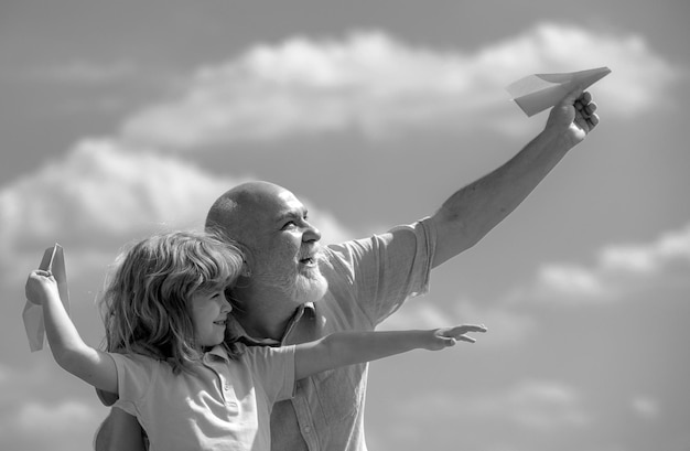 Photo old grandfather and young child grandson with paper plane over blue sky and clouds men generation