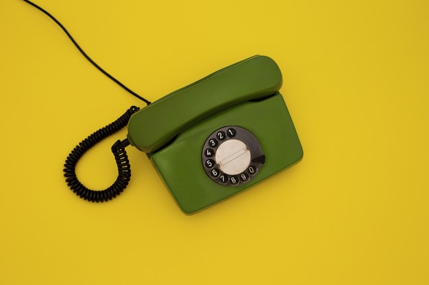 Old green dial phone on yellow