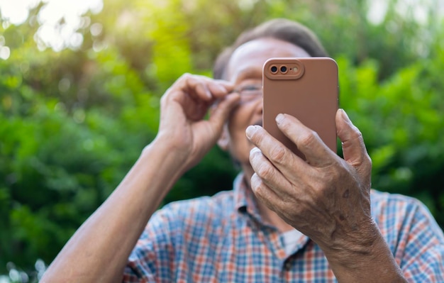 Old grey hair male wearing glasses relaxing using mobile phone outdoor