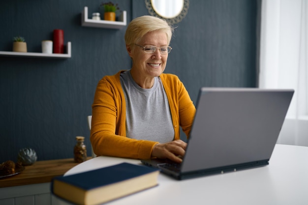 Old grey-haired woman having video conference on laptop greeting talking with children or friends