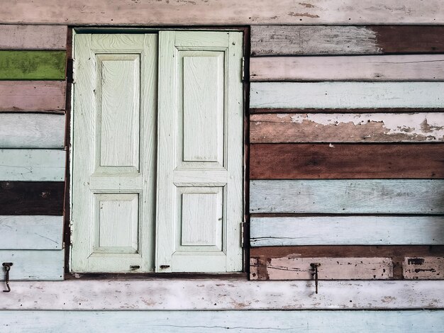 Old grunged wooden window frame painted white vintage with old colourful plywood wall