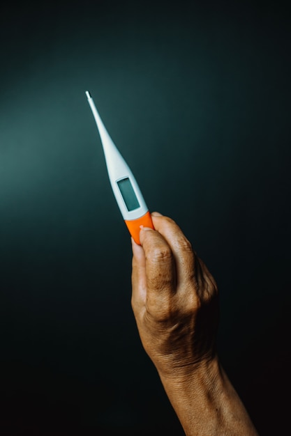 An old hand grabbing a thermometer over a dark background