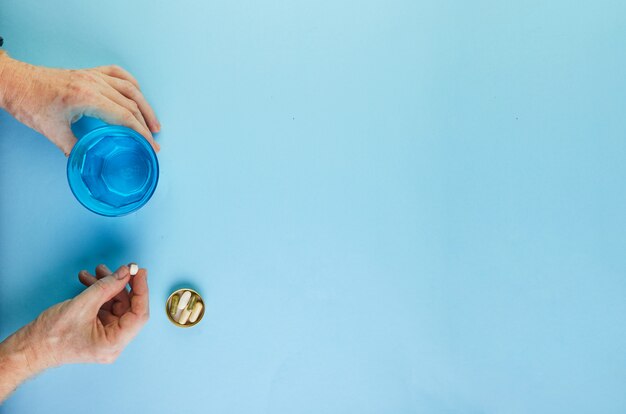 Old hands with pills and a glass of water.