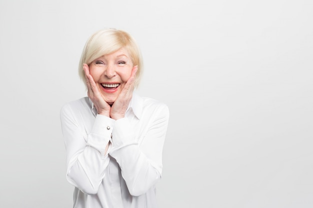 Old but happy woman wears white blouse and showing that she is ery surprised. She has a good luck.