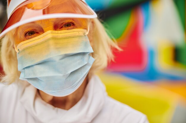 Old, healthy and cheerful lady on a colourful square outdoors wearing mask