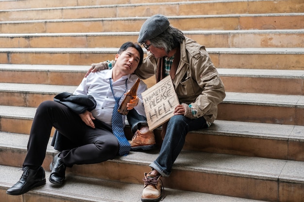 Old homeless people are listening to the problems of businessman with alcohol bottle