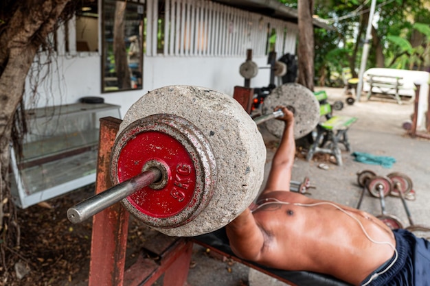 Old homemade barbell and dumbbells made of concrete bucket on the ground a man lifts a homemade barbell in an outdoor gym The concept of sports for the poor