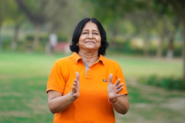 Old Indian lady doing clapping yoga outdoor