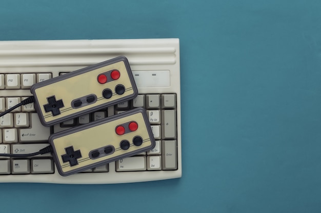 Old keyboard and old-fashioned gamepads on a blue background. Retro gaming. 80s. Top view. Flat lay
