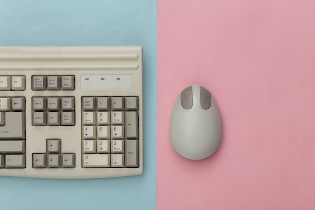 Old keyboard and pc mouse on blue pink background. Top view. Flat lay