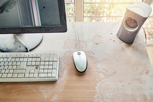 Old keyboard with mouse and broken monitor are on wooden table and covered in thick dust in workshop