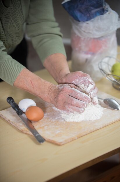 小さなパイを作るおばあさんが机の上で生地をこねる