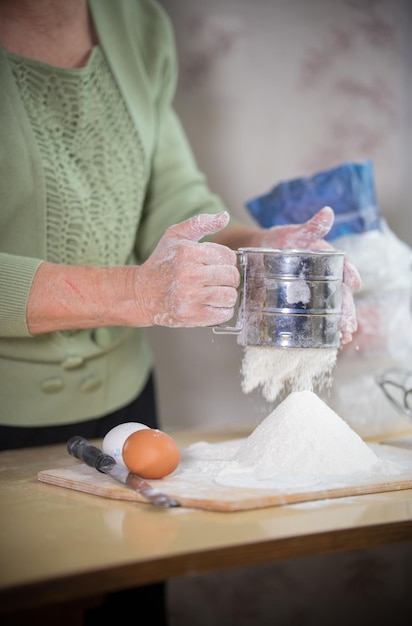 작은 파이를 만드는 노부인 밀가루를 체로 치다 손 클로즈업