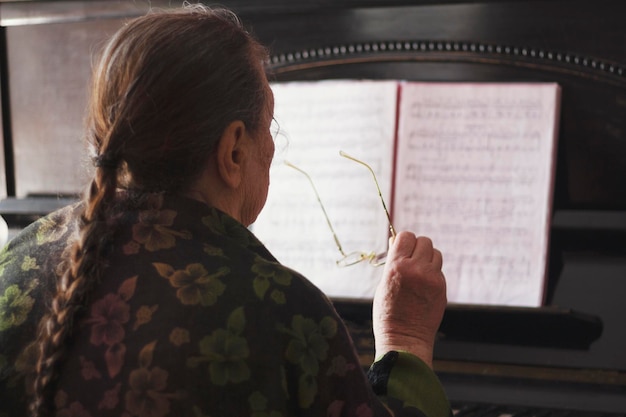 The old lady sitting in front of a piano and a note book with glasses in her hands, active ageing