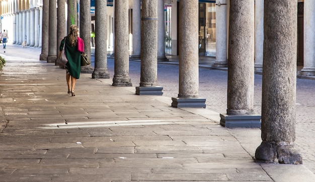 Old lady walking under the typical arcade in Novara