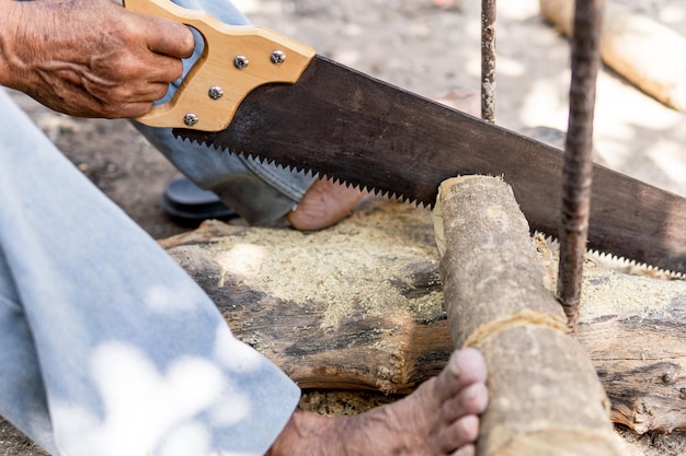 Old latino man chopping wood with a saw