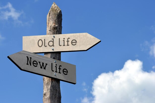 Old life and new life wooden signpost with two arrows sky with clouds