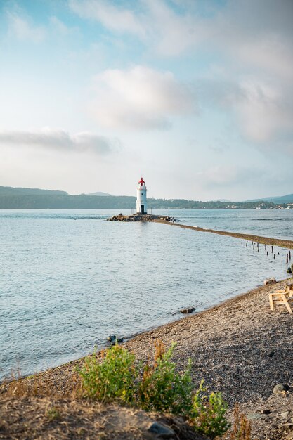 An old lighthouse with a red roof on the seashore. Seascape. Postcard from travel.