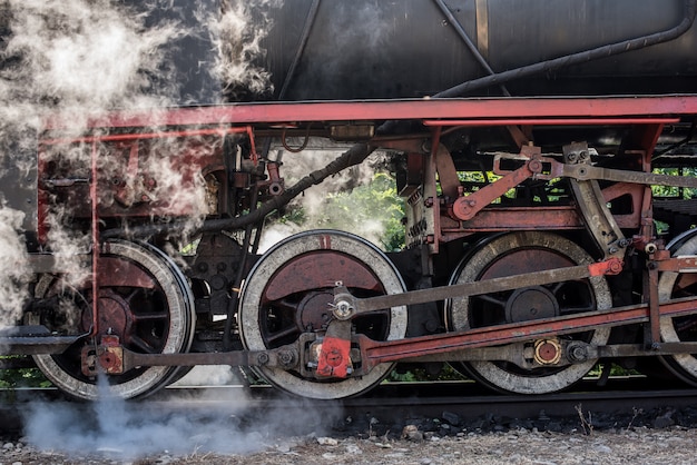 Old locomotive wheels. Historical steam train passes through the deciduous forest.