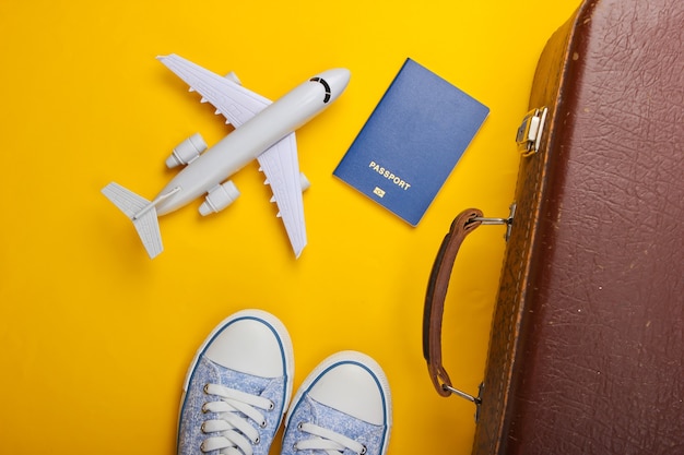 Старый багаж, фигурка самолета, паспорт, кроссовки на желтой поверхности