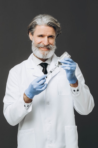 手袋と医療マスクの古い男性医師が注射器を保持しています。