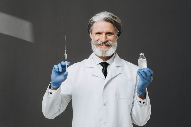 Old male doctor in gloves and medical mask is holding syringe