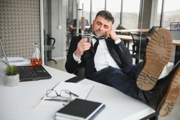 Foto vecchio dipendente maschio che beve alcol sul posto di lavoro