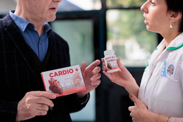 Old man asking pharmacist to explain cardiovascular vitamin prescription instruction in medical retail store. Young pharmaceutical specialist helping elderly customer to select medication analog