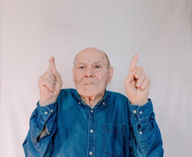 An old man in a blue shirt points up with his index fingers