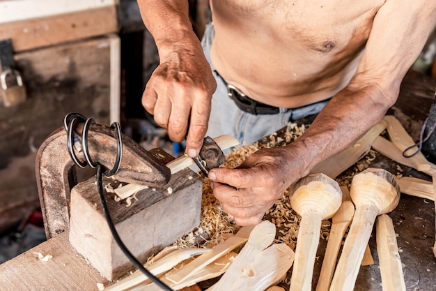 Photo old man carving wooden spoons in the workshop