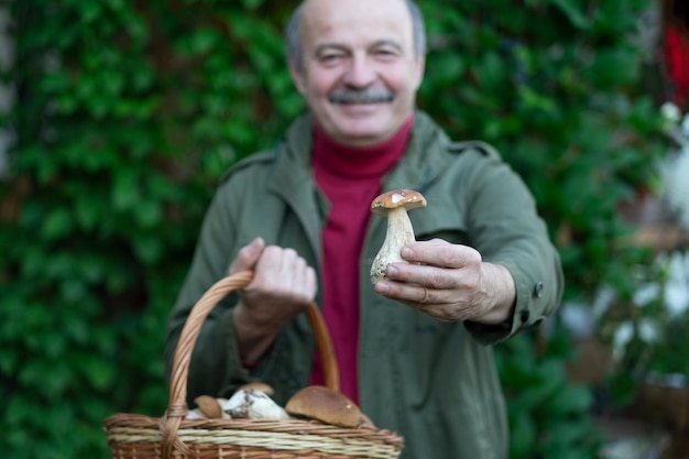 Old man gathers mushrooms showing a cep from basket