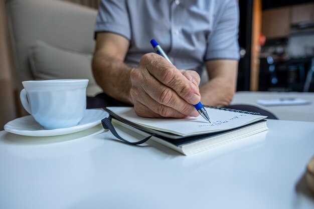 Old man hands writting notes while drinking coffee in living room