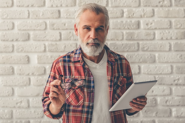 Old man holding a digital tablet and eyeglasses.