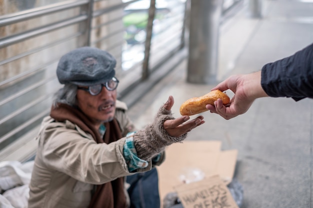 Il vecchio senzatetto allunga la mano per prendere il pane dal donatore sul ponte del corridoio