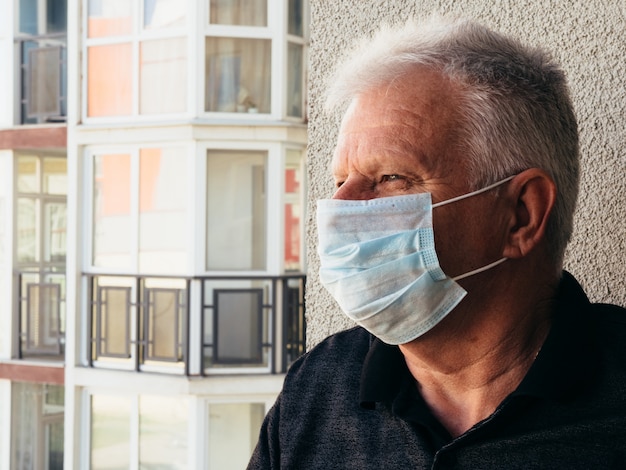 Old man in a medical mask on the balcony of the house.