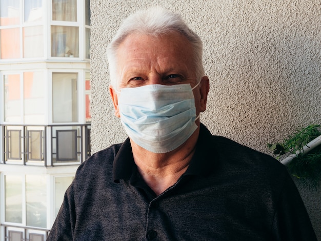 Old man in a medical mask on the balcony of the house.