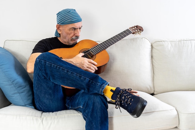 Old Man Practicing to Play Guitar Sitting on Sofa at Home