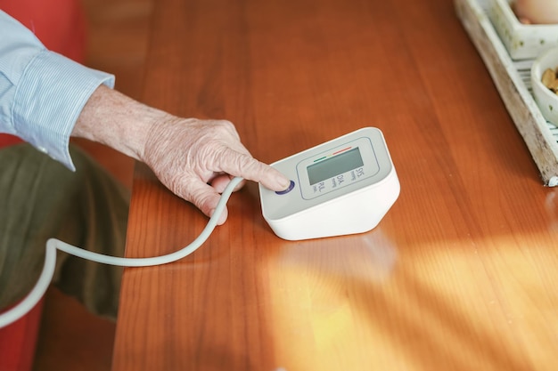 Old man presses the start button to take his blood pressure Health