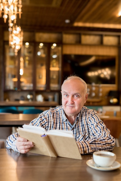 Old man reading a book in a cafe