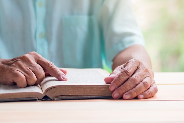 old man reading book on light brown wooden table surface