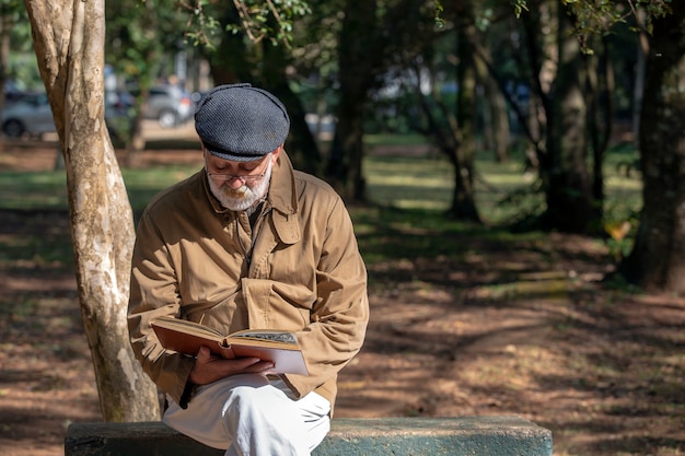 Uomo anziano seduto sulla panchina a leggere un libro