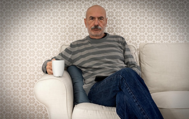 Old man sitting at sofa and drinking coffee from mug