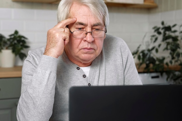 Old man Thinking at Laptop Pensive Mature Grey hair 60s 70s Aged Man Sitting at Table with laptop Thoughtful retired Senior male works online at computer from home Solving Problems with Solutions