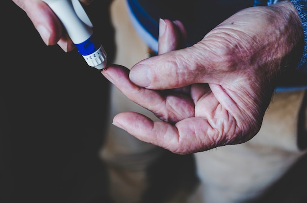 Old man using lancet pen on black 