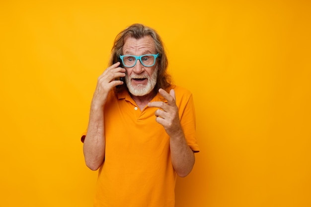 Old man wearing blue glasses yellow shirt talking on the phone cropped view High quality photo