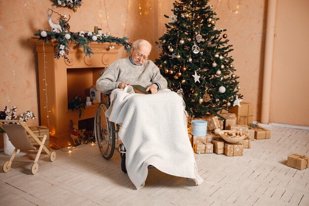 Old man on a wheelchair sitting near christmas tree and\
sleeping