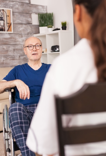 Old man in wheelchair talking with nurse about his medical problem.