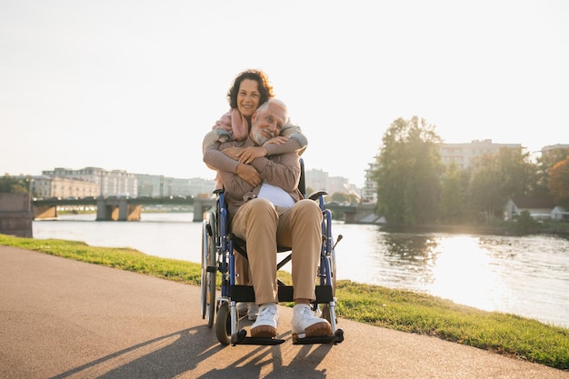 Foto vecchio in sedia a rotelle che cammina con un caregiver donna anziana sulla strada nel parco coppia di famiglie anziane